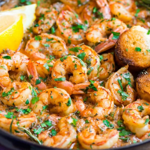 Close-up of Indian-style shrimp in a rich sauce, garnished with parsley, lemon, and toasted bread.