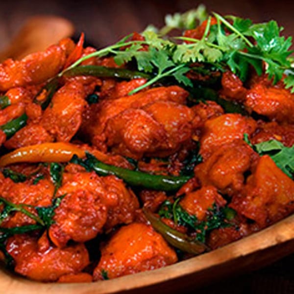 Spicy Indian chicken dish with red chili sauce, green peppers, and fresh cilantro in a wooden bowl.