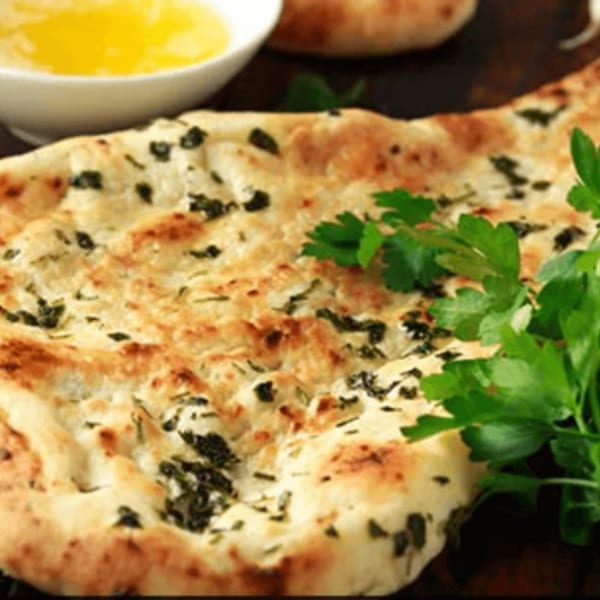 Indian naan bread with herbs and a side of melted butter, garnished with fresh parsley.