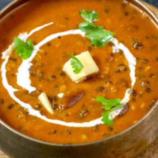 A bowl of Indian dal makhani, garnished with cream, butter, and fresh cilantro.