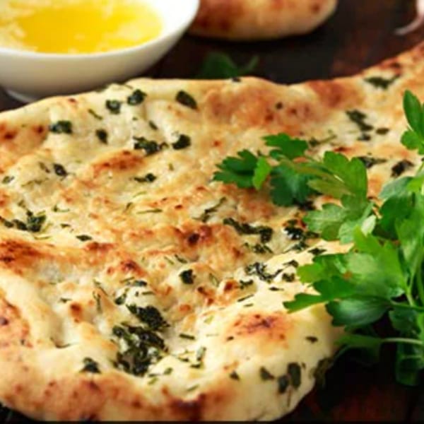 Garlic naan bread with fresh parsley and a small bowl of melted butter.