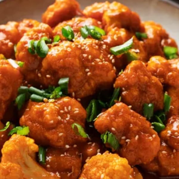Close-up of orange-glazed Indian cauliflower bites, garnished with sesame seeds and green onions.
