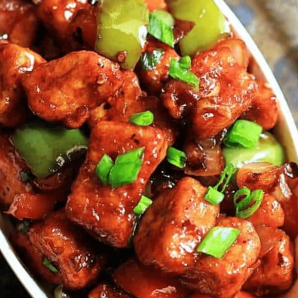 Close-up of Indian chili paneer with green bell peppers and scallions in a white dish.
