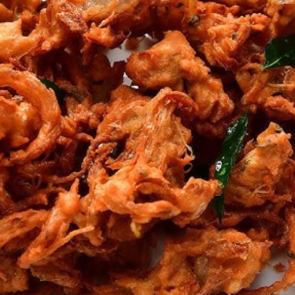 Close-up of crispy, golden-brown Indian onion pakoras with green herb garnishes.